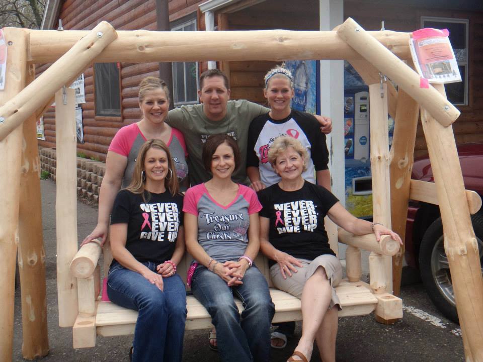 Group of people posing on a wooden swing in front of a building.